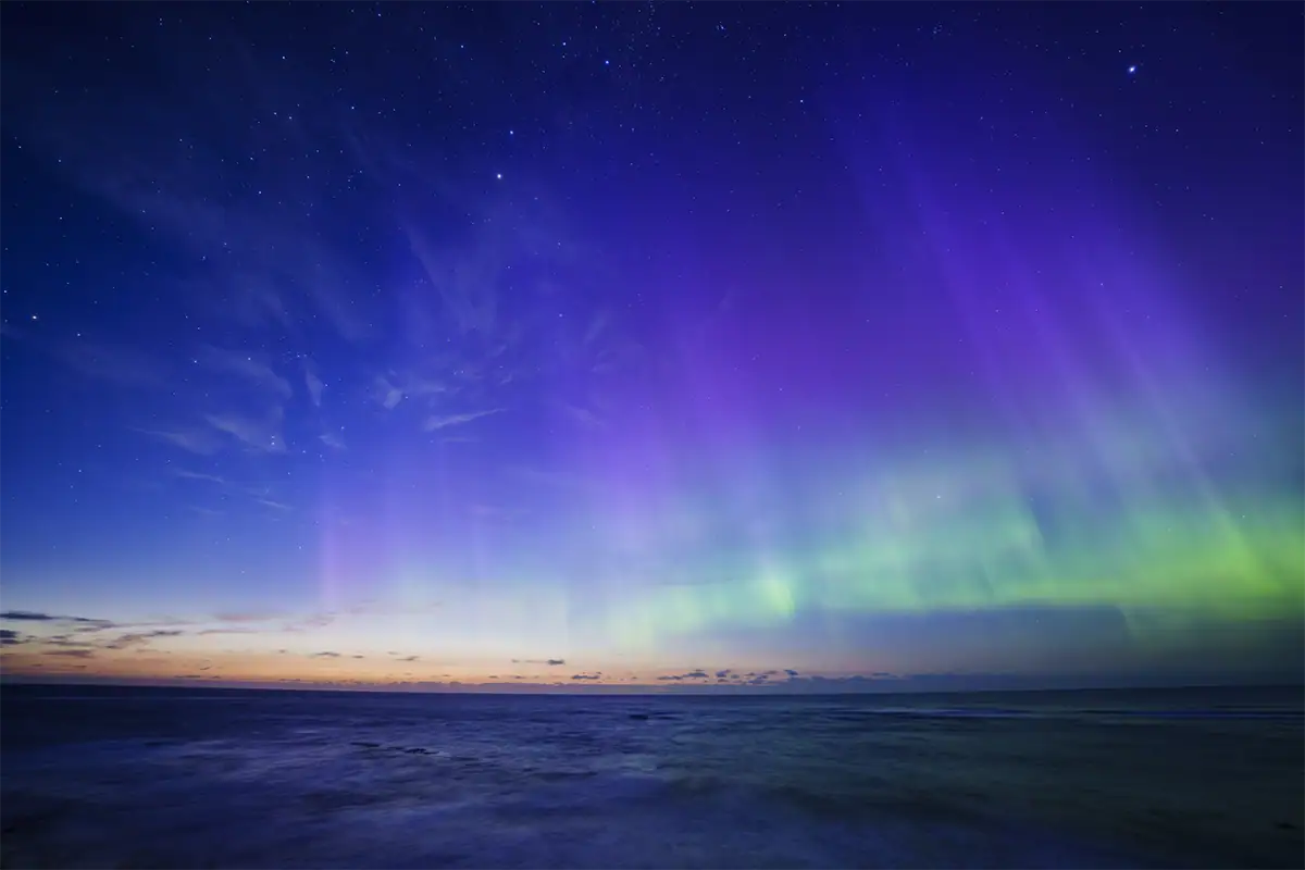 Une aurore violette et verte s'étendant dans le ciel au-dessus de l'océan avant l'aube en Nouvelle-Zélande, photographiée avec le Tamron 12-20 mm F2,8.