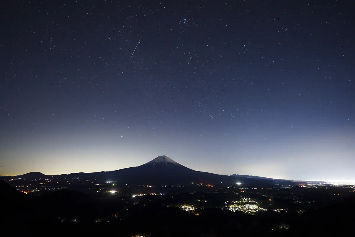 Une étoile filante des Géminides traversant le ciel au-dessus du mont Fuji et des hauteurs d’Asagiri, sous un ciel nocturne parsemé d’étoiles, photographiée avec le Tamron 12-20 mm F2,8.