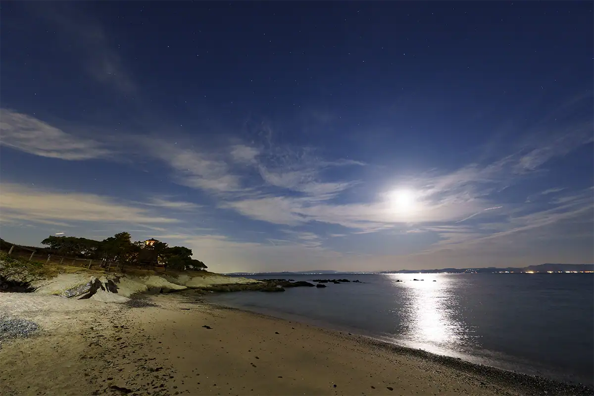 Une lune éclatante au-dessus d'un paysage nocturne côtier, utilisée pour évaluer les images fantômes et les reflets avec le Tamron 12-20 mm F2,8.