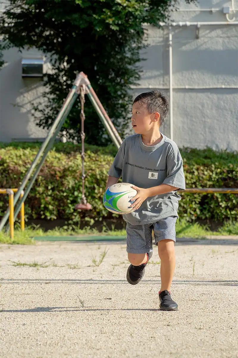 Criança correndo ao ar livre segurando uma bola, fotografada com a Tamron 25-200 mm F2.8-5.6 G2.