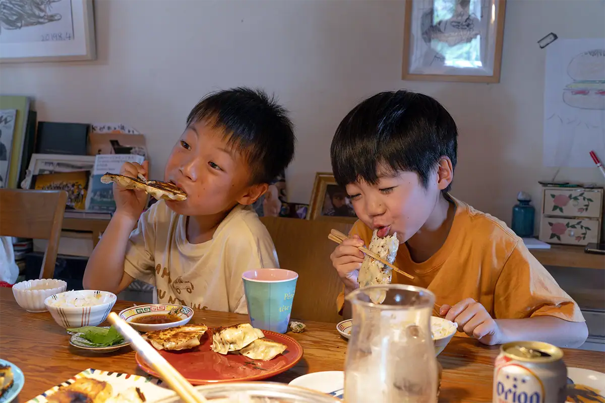 Duas crianças comendo gyoza caseiro juntas à mesa de jantar durante uma reunião familiar informal.