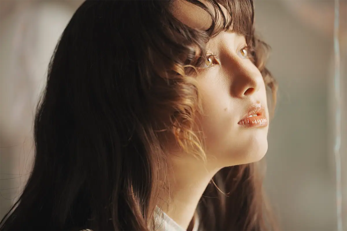 Portrait of a woman beside a window with soft directional light illuminating her face and creating gentle shadows.