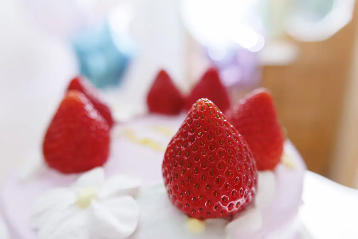 Close-up of fresh strawberries arranged on top of a white birthday cake with colorful decorations softly blurred behind them.