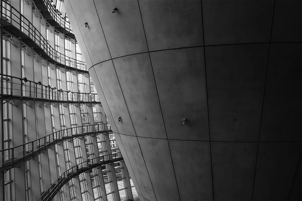 Black-and-white architectural composition featuring a curved concrete wall beside repeating glass windows and walkways.
