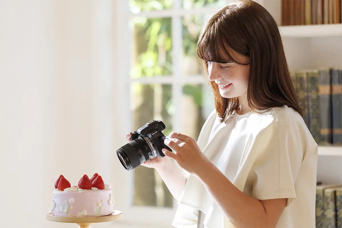 Woman holding a Canon camera with the Tamron 16-50mm F2.8 while photographing a birthday cake indoors.