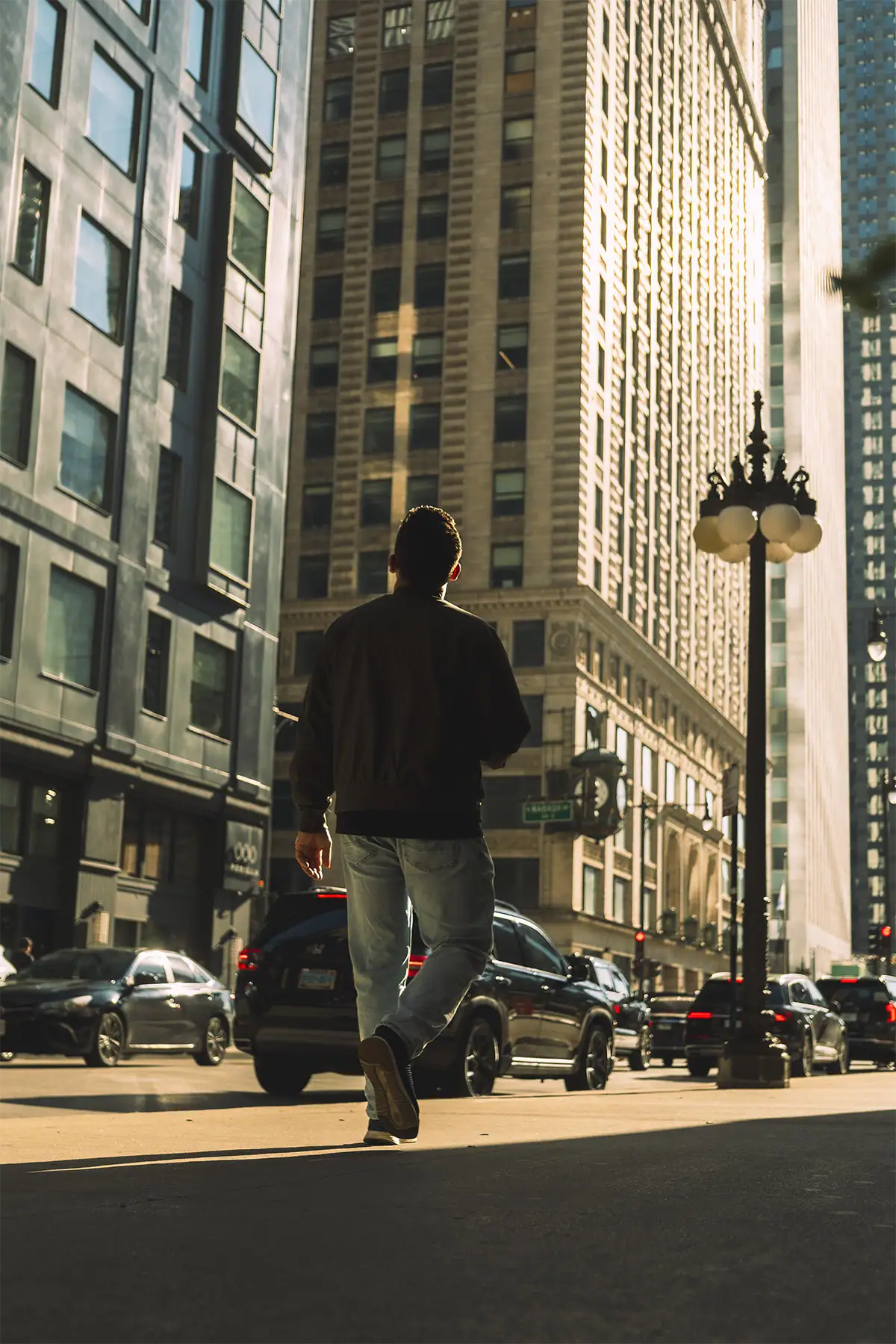 Pedestrian walking through late-afternoon sunlight between tall Chicago buildings, photographed at 28mm.