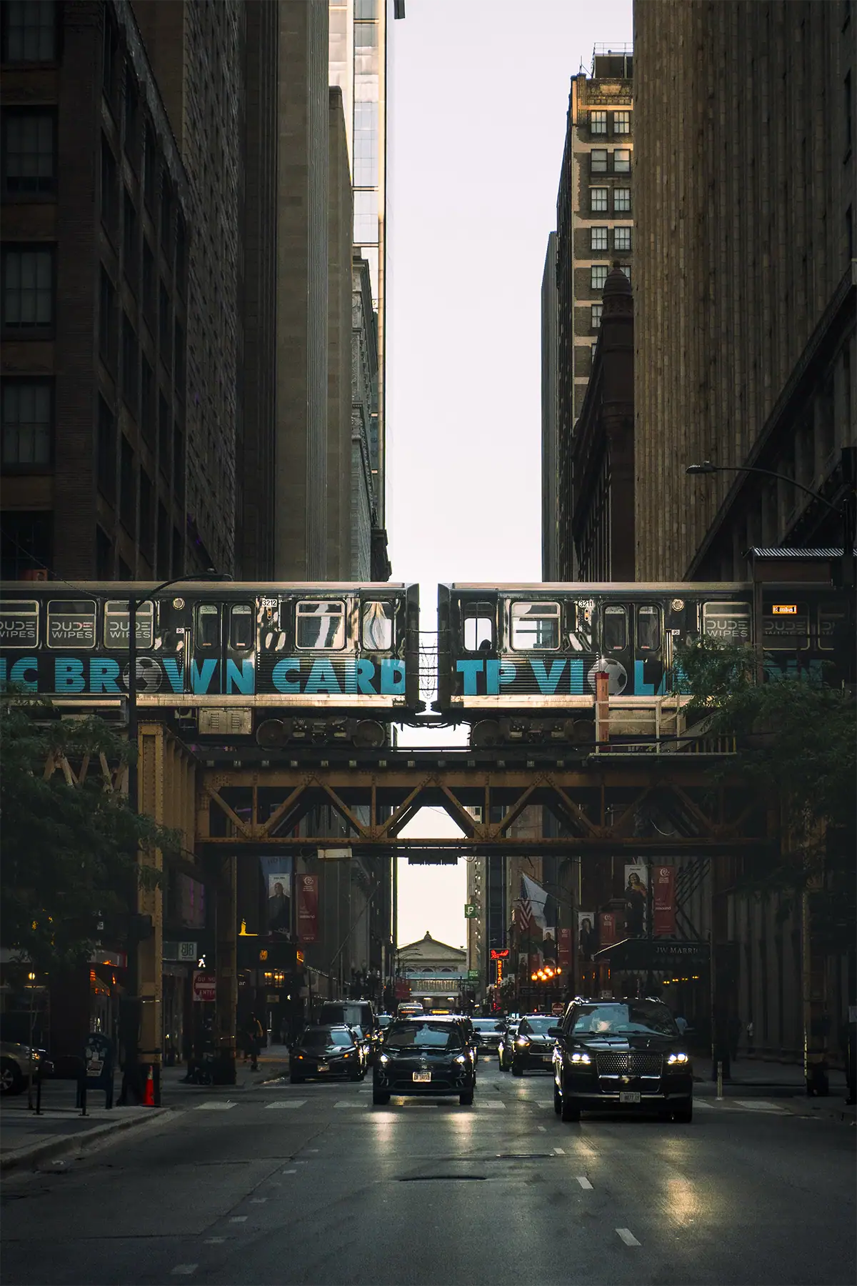 Chicago elevated train passing above downtown traffic between tall buildings, photographed at 50mm.