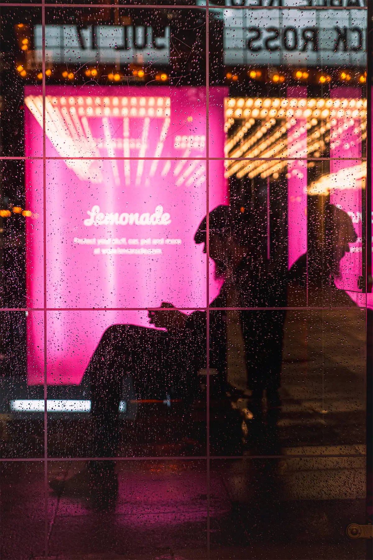 Raindrops sharply focused on glass with a silhouetted person and colorful Chicago lights blurred behind them at 50mm F2.8.