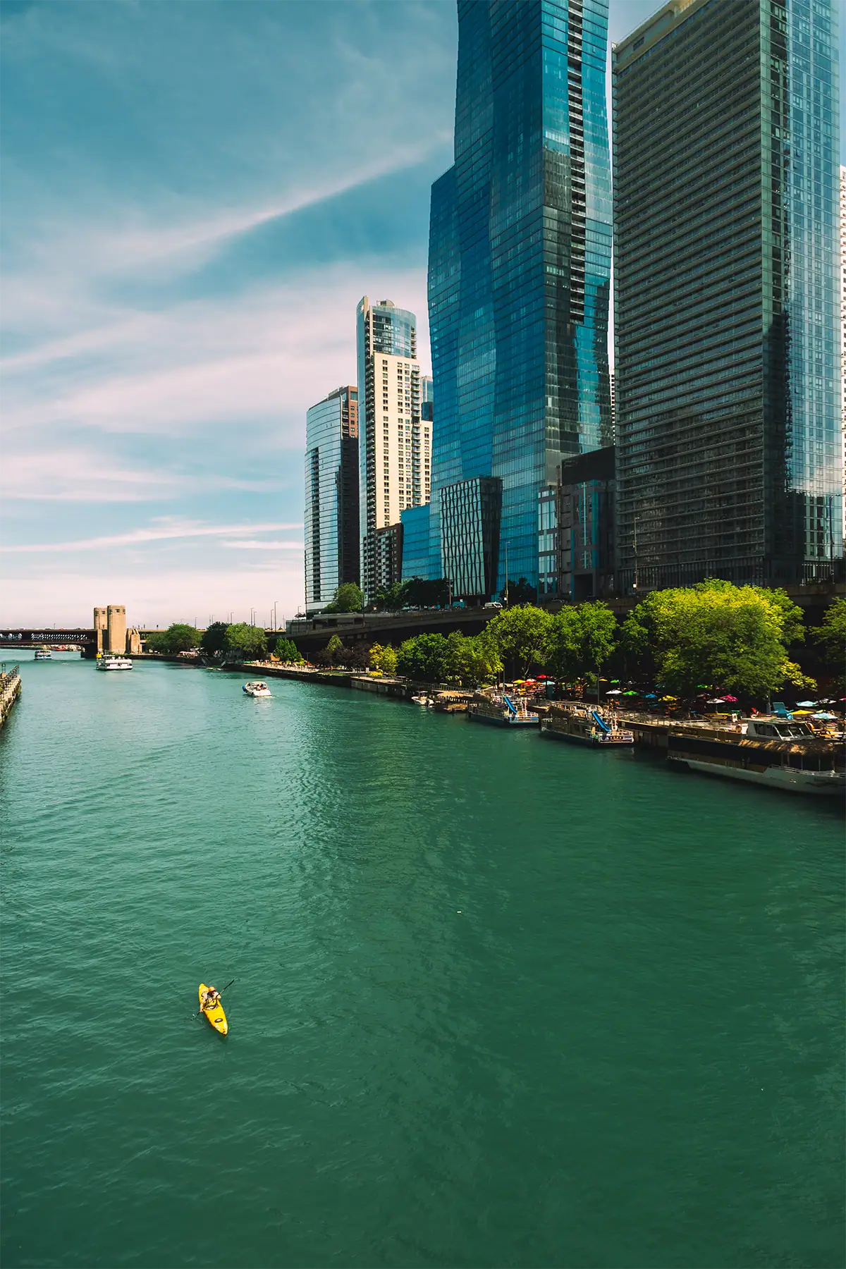 Yellow kayak on the Chicago River surrounded by water, trees, and towering modern skyscrapers, photographed at 16mm.
