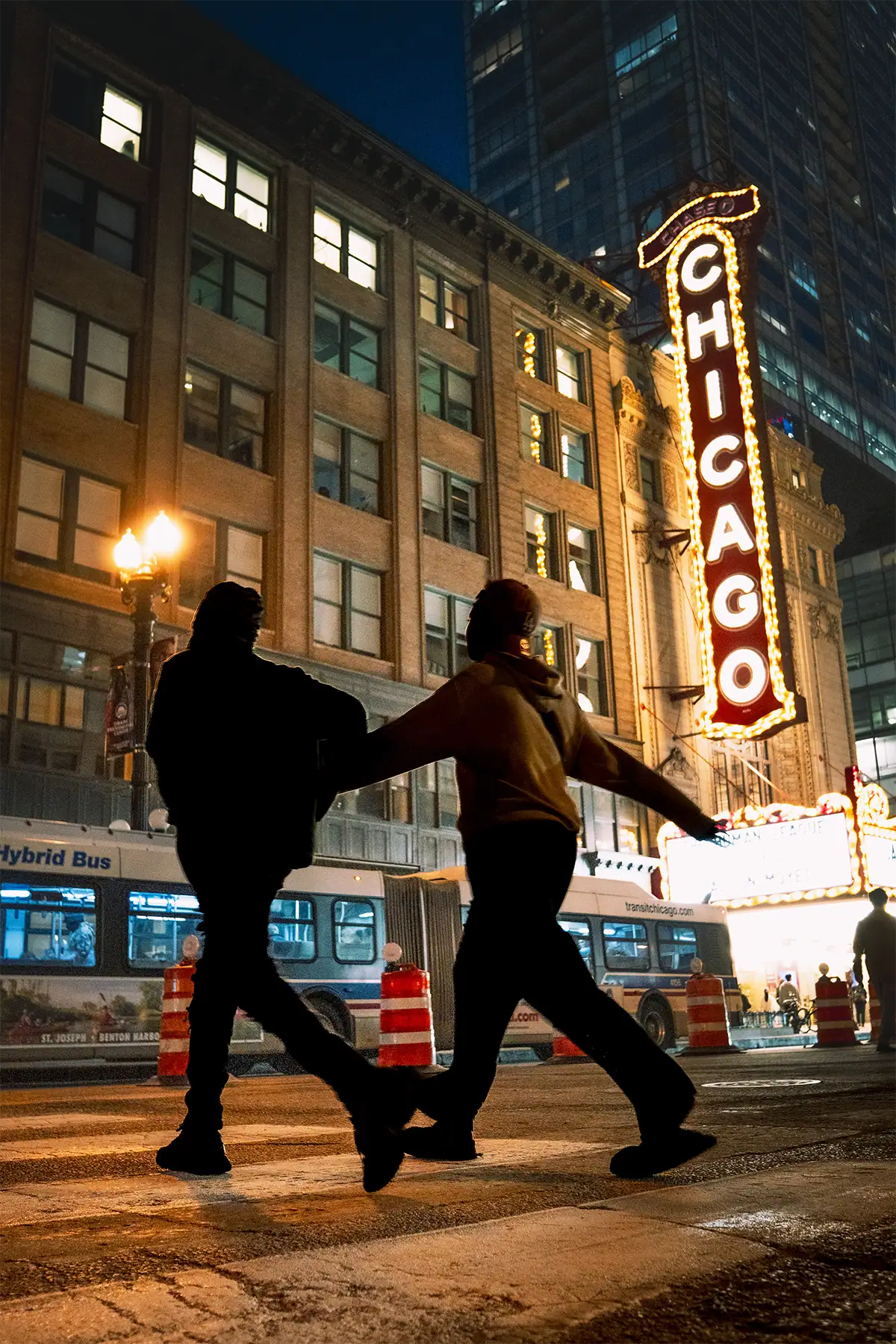 Two pedestrians crossing a Chicago street at night beneath the illuminated Chicago Theatre sign, photographed at 22mm.