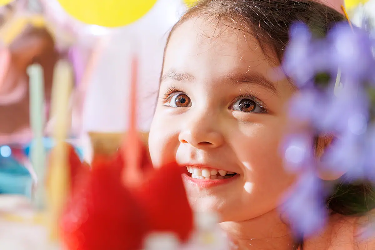 Close portrait of a smiling child with soft colorful birthday decorations blurred in the foreground and background.