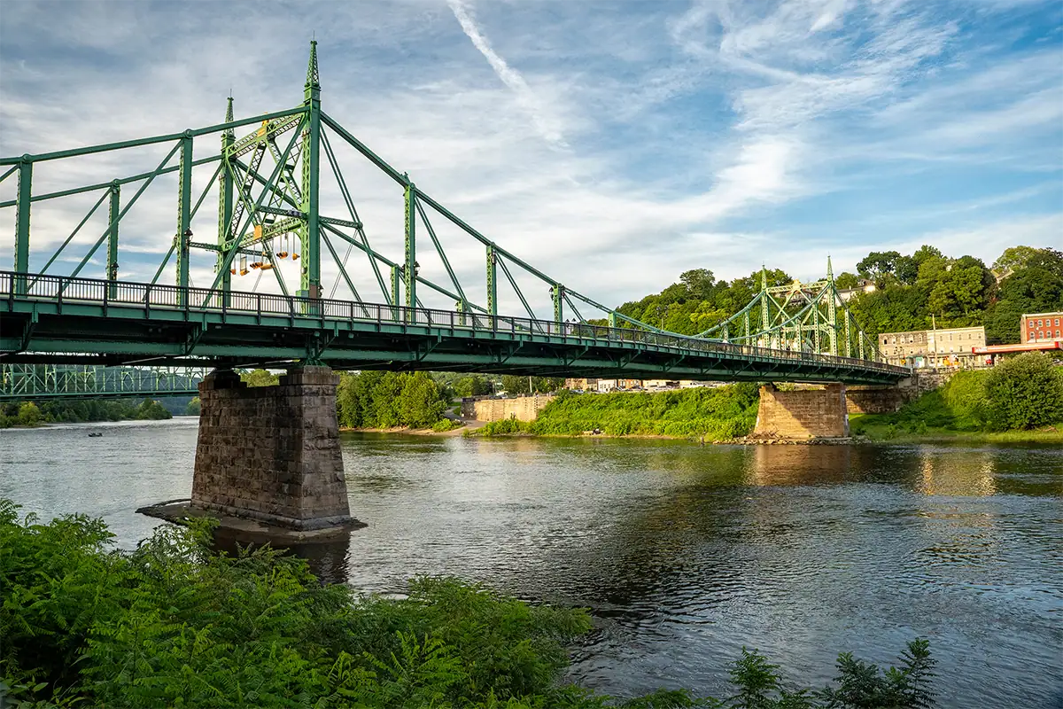 Green steel bridge spanning a river in Easton, Pennsylvania, beneath a blue sky with wispy clouds.