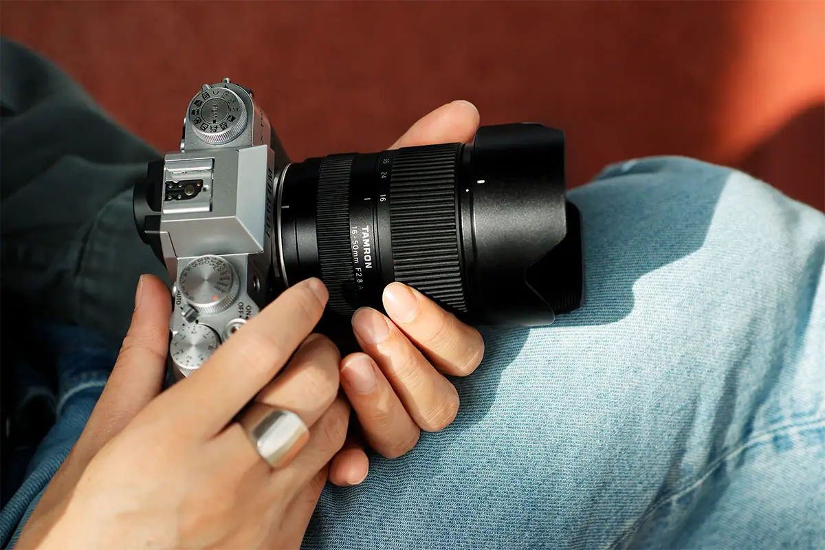 Person holding a Fujifilm camera fitted with the compact Tamron 16-50mm F2.8 lens.