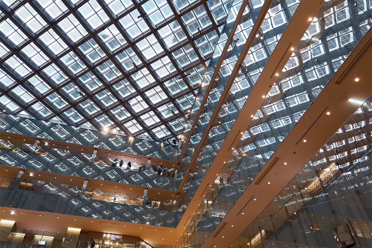 Upward view of a geometric glass-and-steel atrium with repeating windows and warm interior lights.