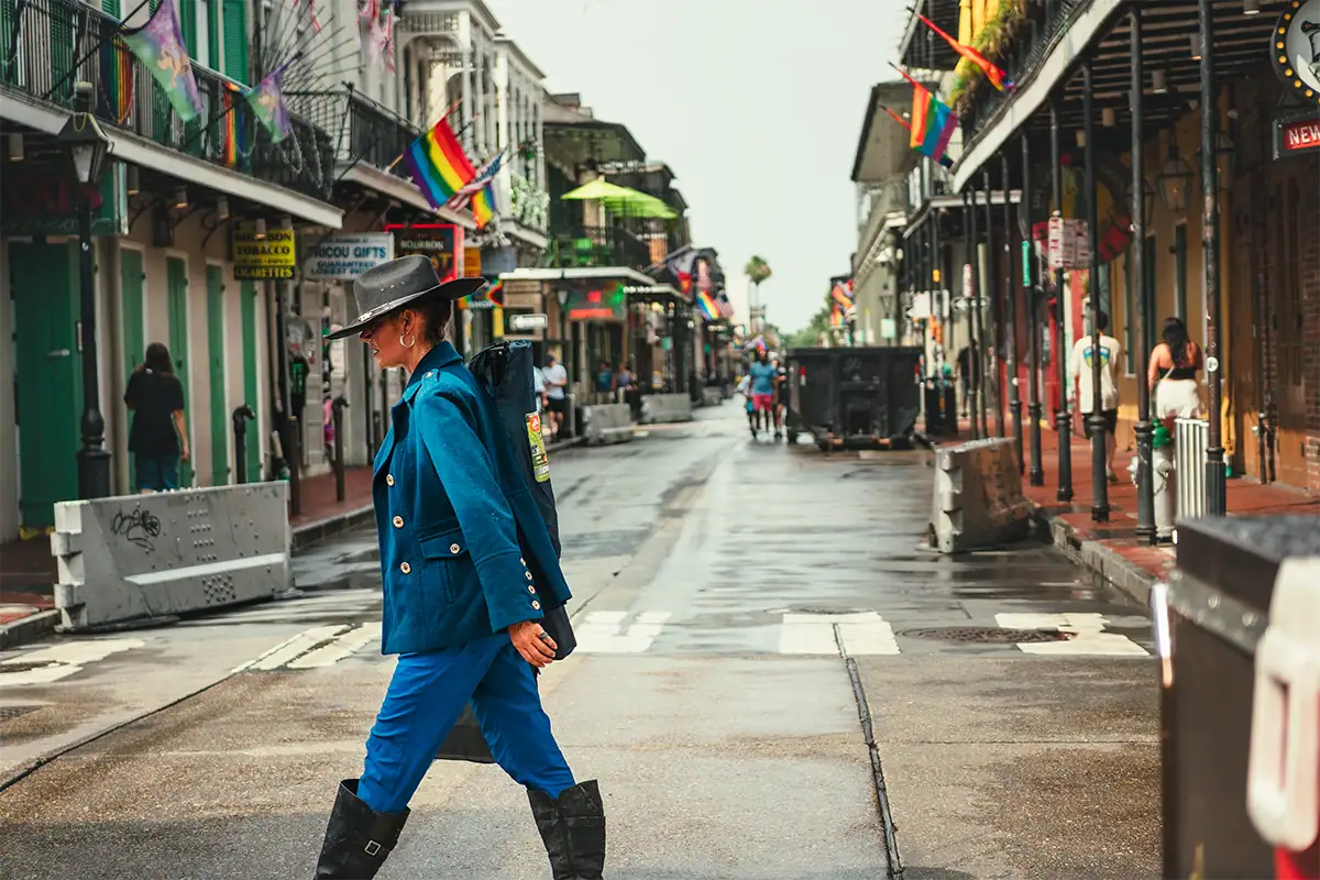 Woman in a vivid blue suit crossing a New Orleans street lined with colorful buildings and flags, photographed at 46mm.