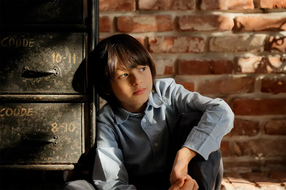 Child seated beside a brick wall in warm light, photographed at 70mm with the Tamron 17-70mm F2.8 for Canon RF.