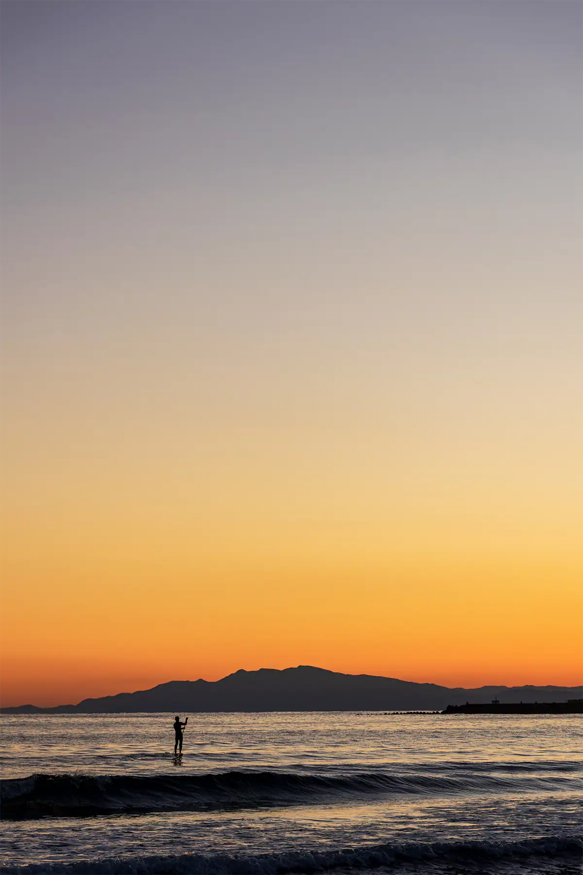 Distant figure standing in the sea beneath an orange sunset sky, photographed at 70mm with the Tamron 17-70mm F2.8.
