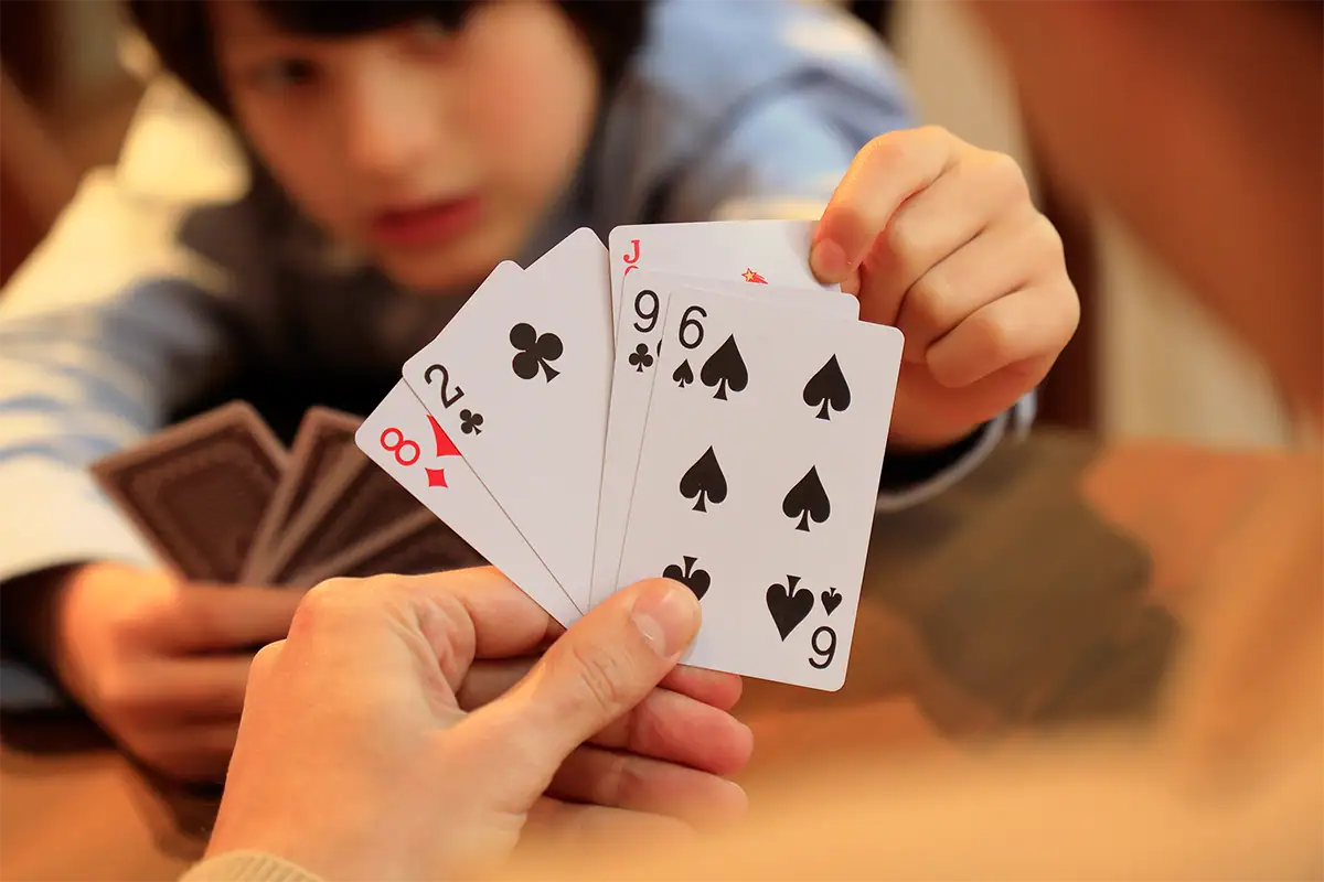 Child playing cards indoors with hands and cards in the foreground, photographed at 70mm F2.8 with the Tamron 17-70mm.