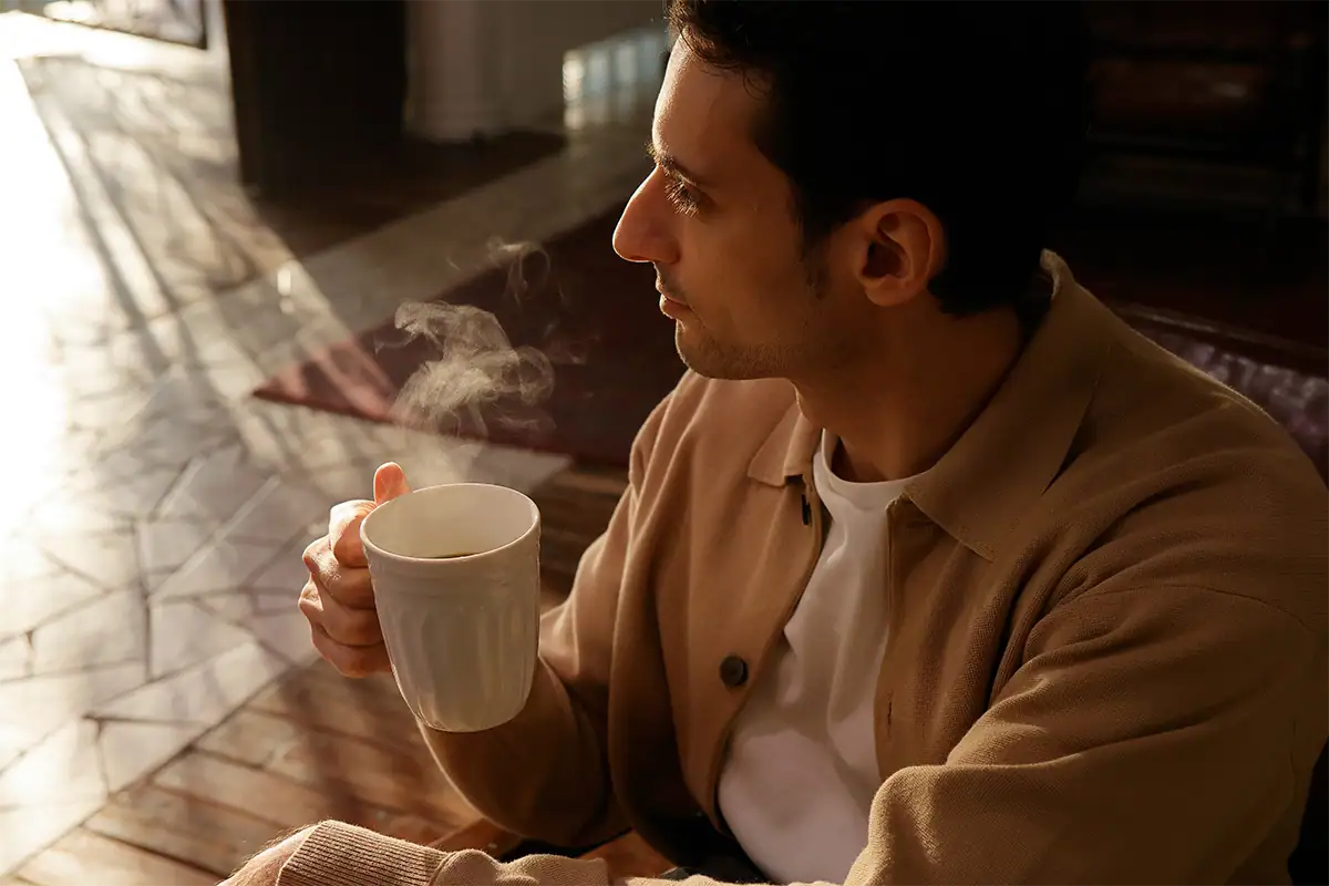 Man holding a steaming cup beside a sunlit window, photographed at 27mm with the Tamron 17-70mm F2.8.
