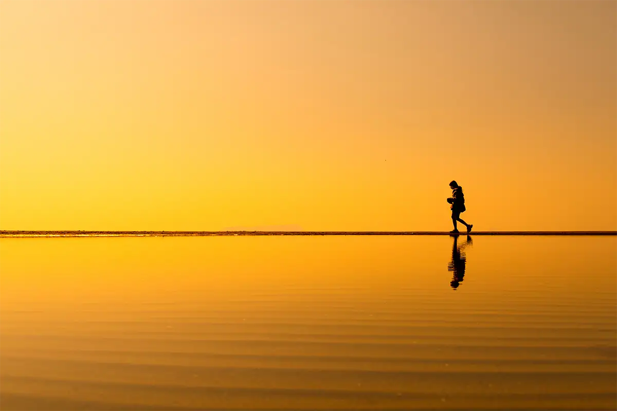 Silhouetted traveler walking beside calm water beneath a golden sunset in Shikoku, Japan, photographed with the Tamron 17-70mm F2.8 for Fujifilm X