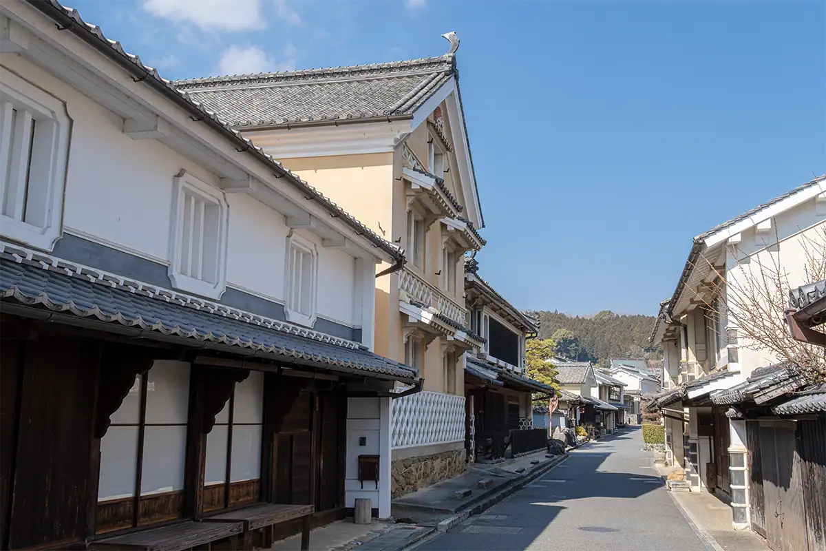 Historic merchant street in Uchiko, Ehime, lined with traditional Japanese buildings under a blue sky, photographed with the Tamron 17-70mm F2.8 for Fujifilm X.
