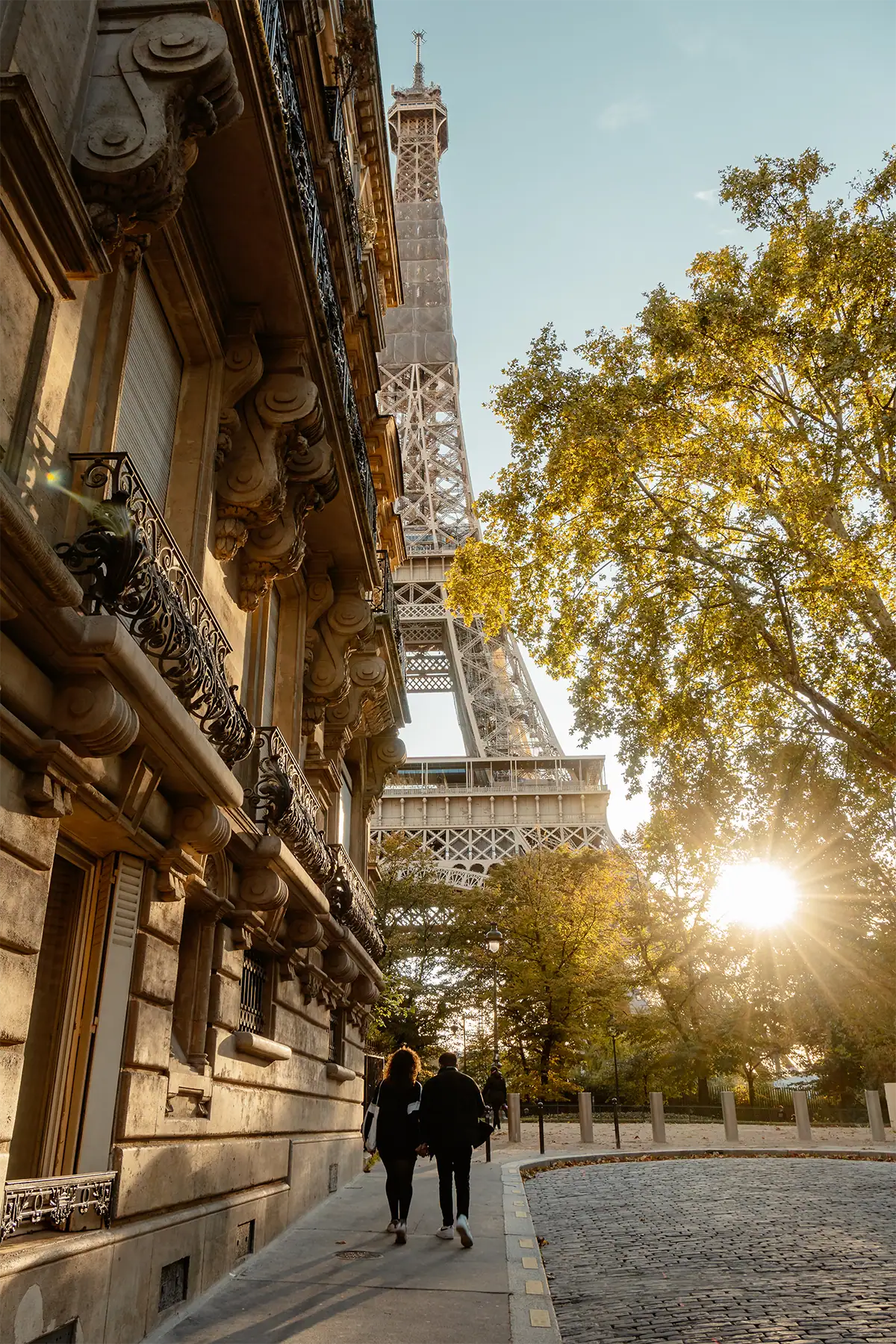 La Torre Eiffel se alza entre un edificio de apartamentos de París y los árboles otoñales, bajo la cálida luz del atardecer, fotografiada con el Tamron 17-70 mm F2.8 para Sony E.