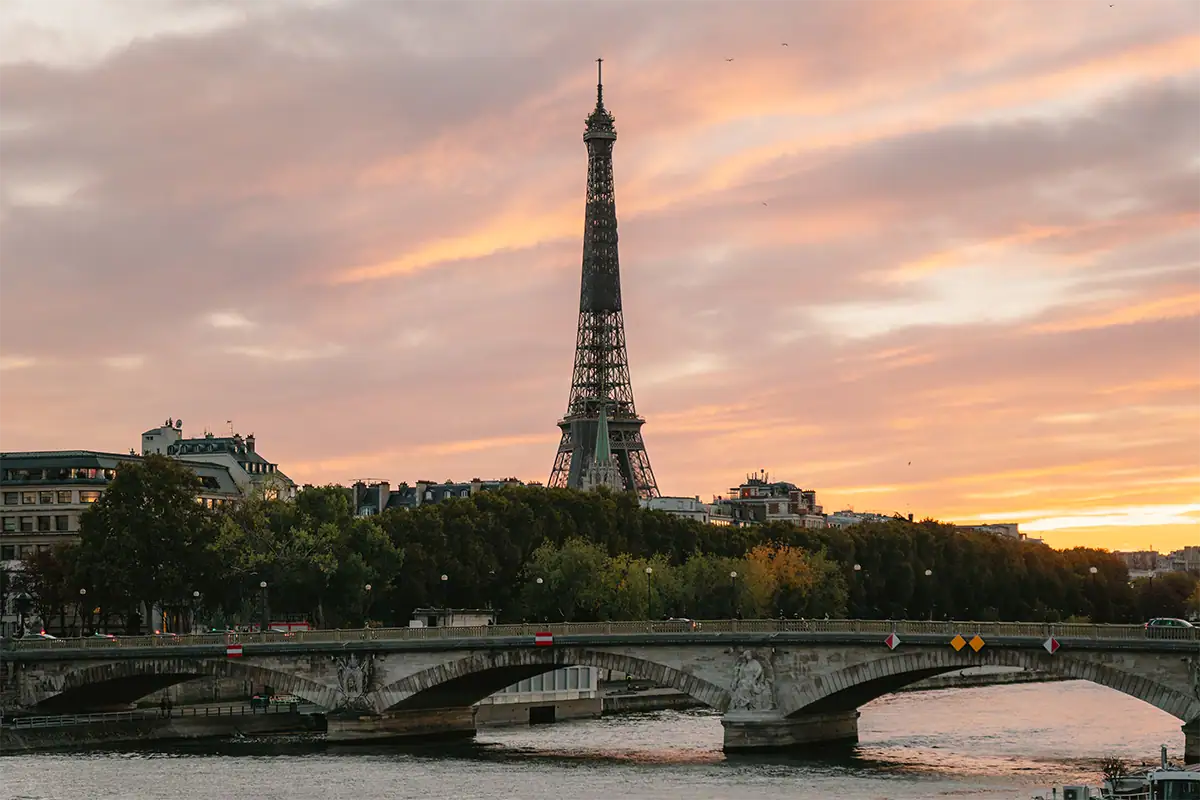 La Torre Eiffel sobre un puente del río Sena, bajo un cielo anaranjado y rosado al atardecer en París, fotografiada con el Tamron 17-70 mm F2.8.