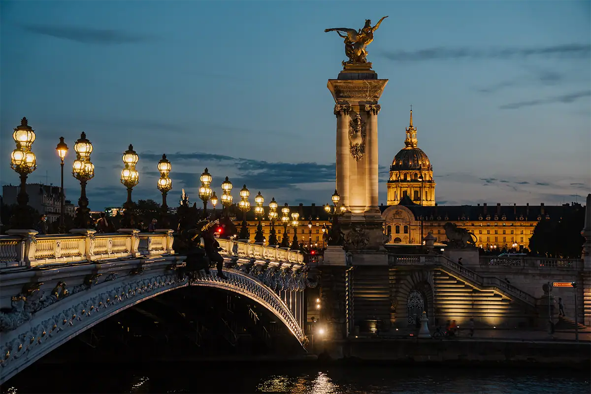 El Puente Alexandre III iluminado durante la hora azul, con Les Invalides resplandeciendo al fondo en París, fotografiado con el Tamron 17-70 mm F2.8 para Sony E.