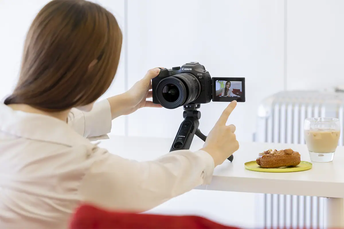 Photographe utilisant un appareil photo sans miroir équipé d'un objectif Tamron, en train de vérifier l'écran LCD arrière pendant un tournage vidéo.