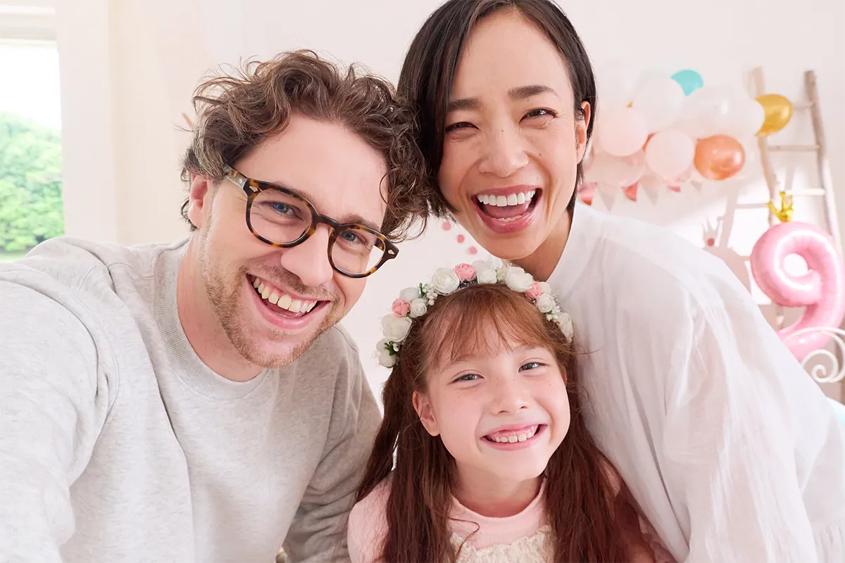 Une famille de trois personnes souriantes posant ensemble lors d'une fête organisée en intérieur, photographiée avec l'objectif Tamron 16-50 mm F2.8 A pour monture Nikon Z.