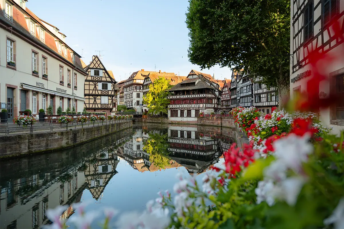 Historic half-timbered buildings reflected in a canal in Strasbourg, France, with colorful flowers in the foreground, photographed with the Tamron 16-50mm F2.8 A for Nikon Z mount.