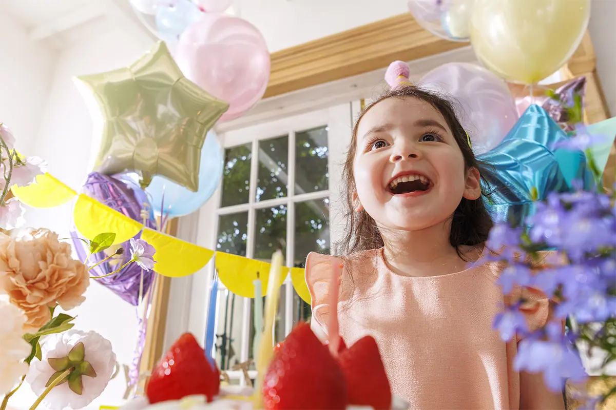 Portrait spontané et joyeux d'une jeune fille souriante, entourée de ballons d'anniversaire colorés et de fleurs, illustrant la photographie de famille et de mode de vie réalisée avec l'objectif Tamron 16-50 mm F2.8 A.