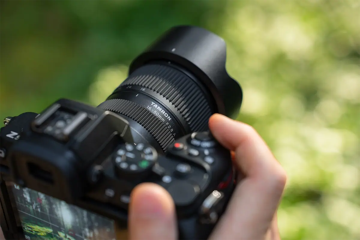 Close-up de uma lente Tamron 16-50 mm F2.8 A montada em uma câmera sem espelho Nikon Z, segurada por um fotógrafo ao ar livre.