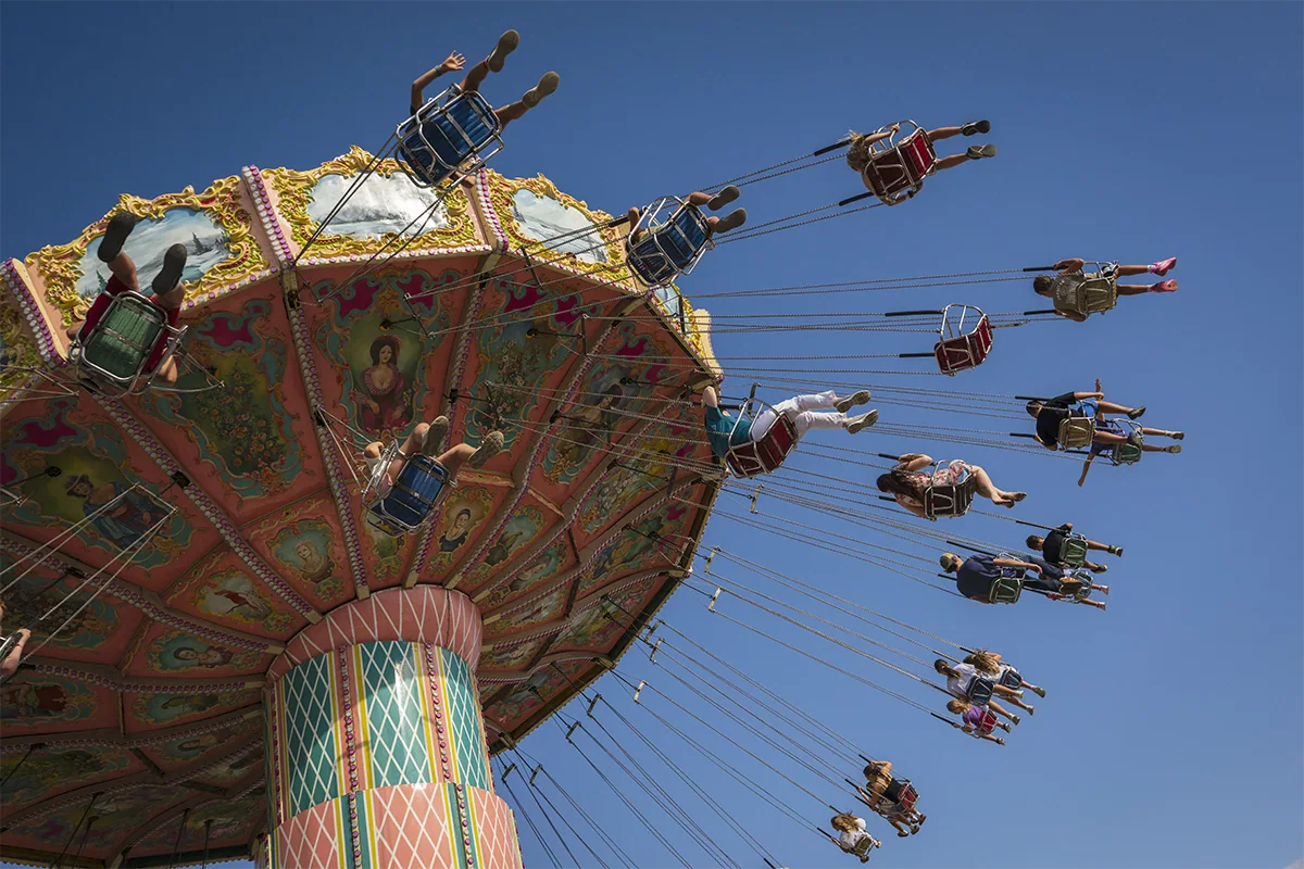 Colorful amusement park swing ride with people suspended high against a clear blue sky, photographed with the Tamron 20-40mm F2.8 for Nikon Z mount.