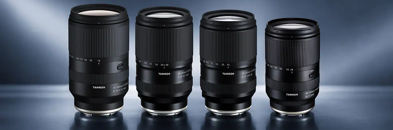 Quatro lentes zoom multifuncionais da Tamron — 18-300 mm, 25-200 mm G2, 28-200 mm e 28-300 mm — expostas juntas contra um fundo azul-acinzentado de estúdio.
