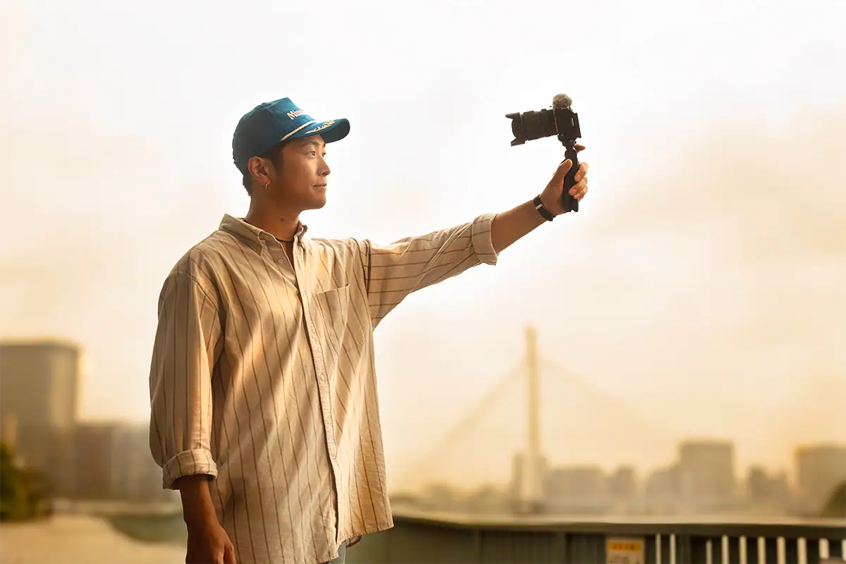 Content creator filming a vlog outdoors with a mirrorless camera and Tamron lens mounted on a handheld grip