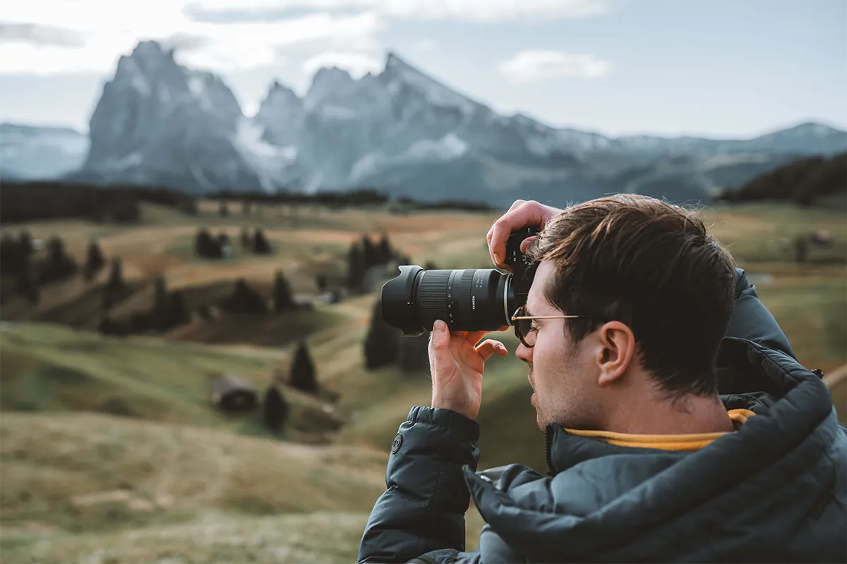 Photographer using a Tamron 17-70mm F2.8 zoom lens on a mirrorless camera to capture a scenic mountain landscape, demonstrating Tamron standard zoom versatility for outdoor and travel photography.